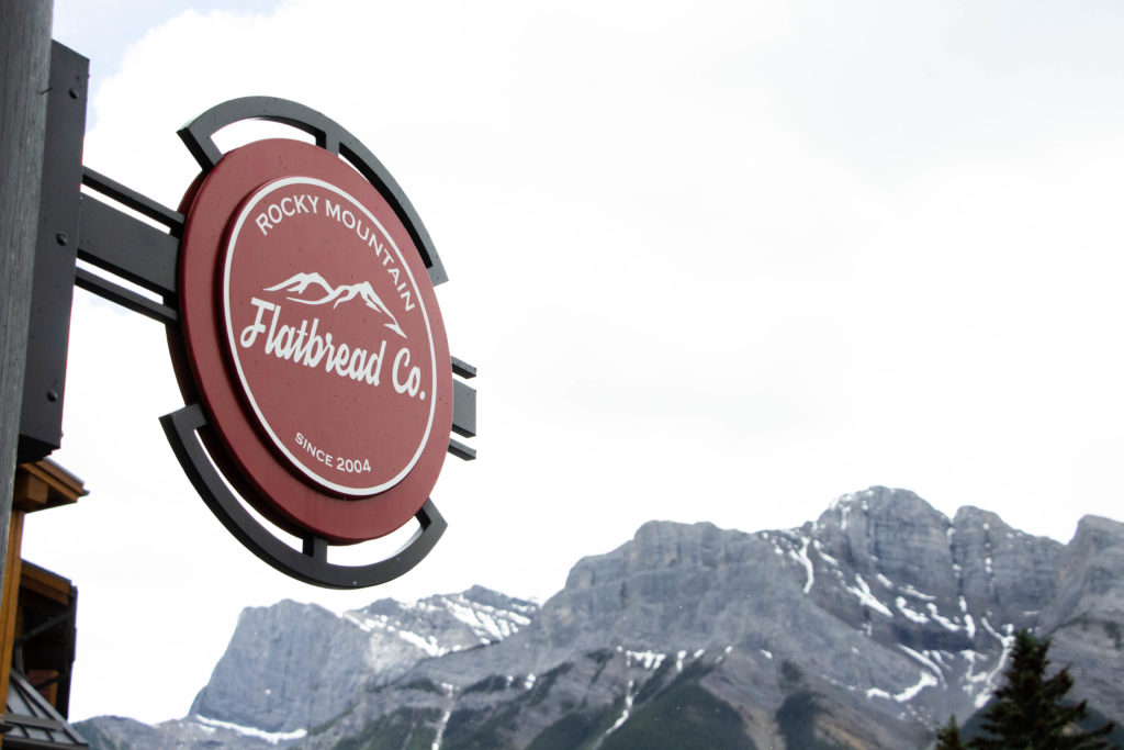 Rocky Mountain Flatbread Co. sign with mountains in background, Canmore restaurant