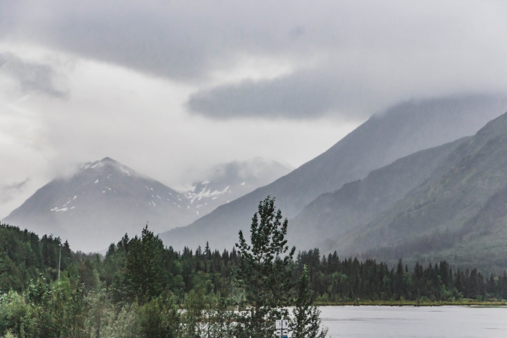 cloudy foggy mountains beside lake and green trees on seward highway alaska