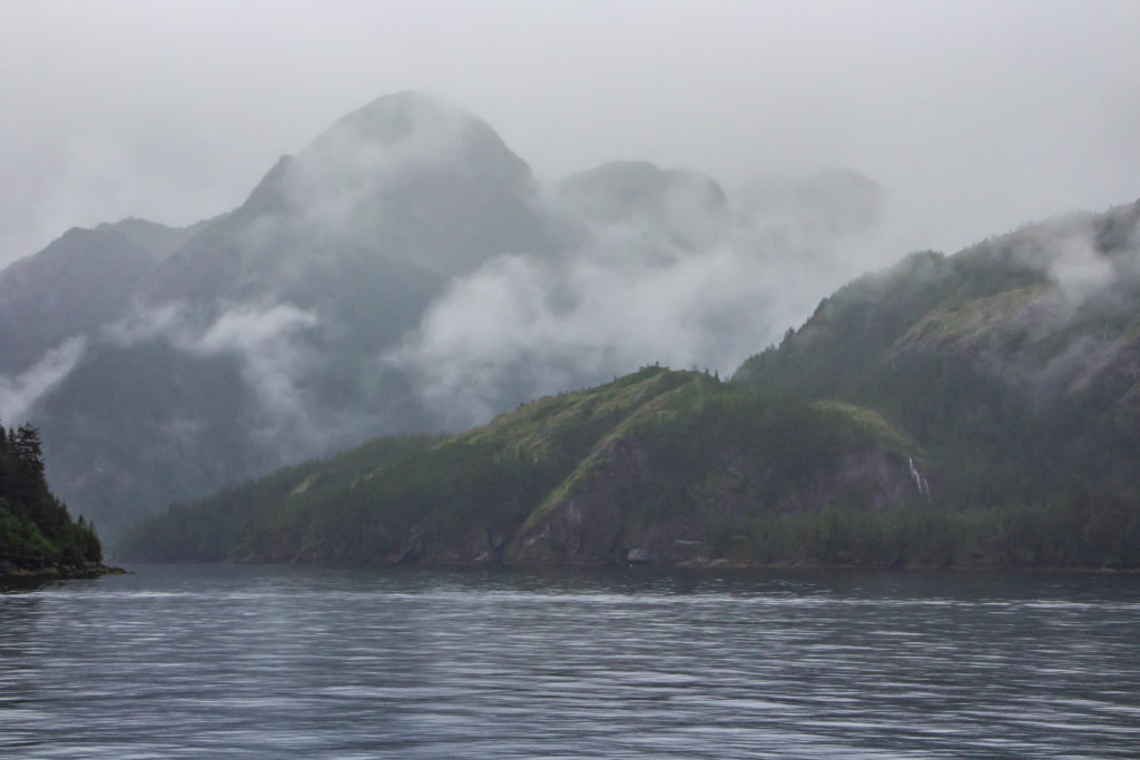 cloudy foggy mountains beside blue ocean water in seward alaska