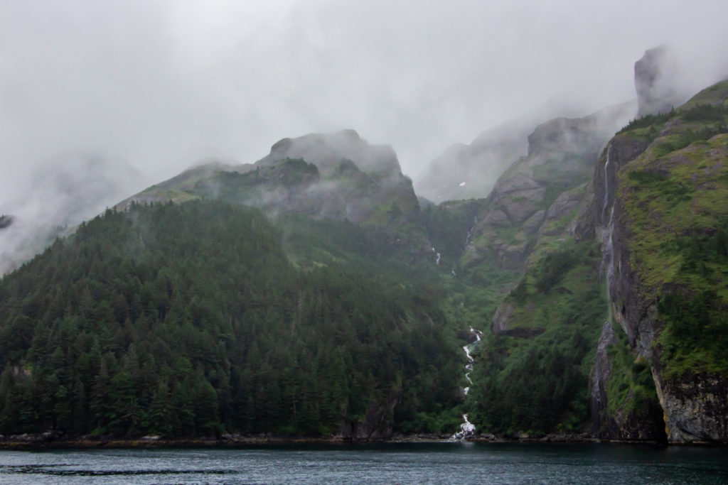 foggy cloudy green mountains beside blue ocean water with waterfalls in Seward alaska