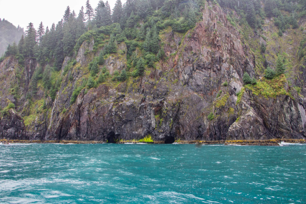caves and green moss at spire cove seward alaska with turquoise ocean water and mountains