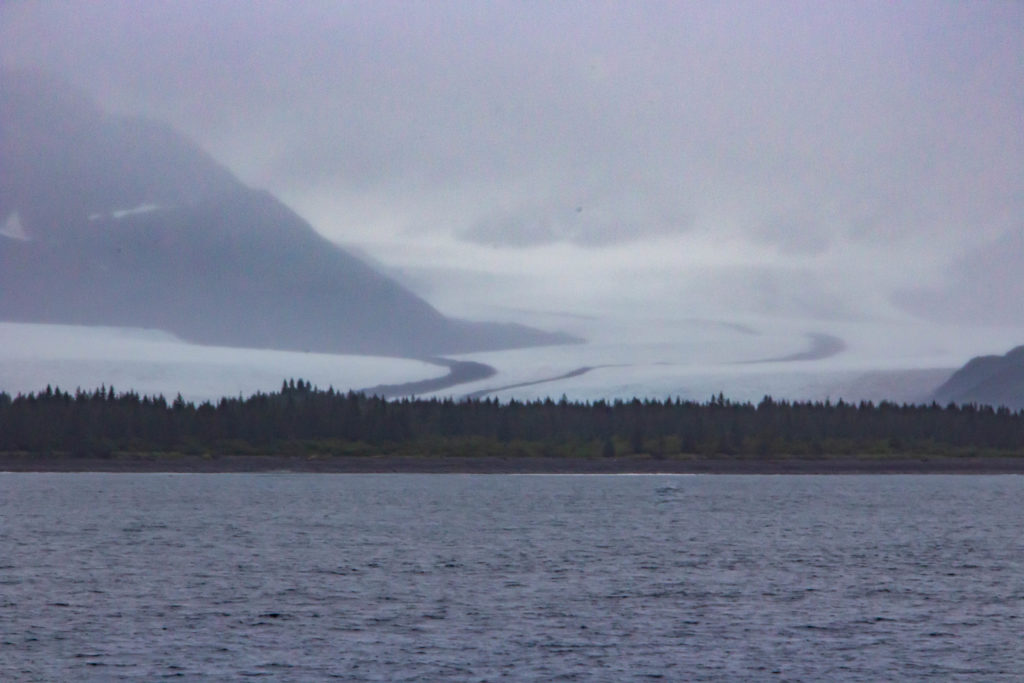 Bear Glacier and cloudy mountains beside ocean water in Seward, Alaska