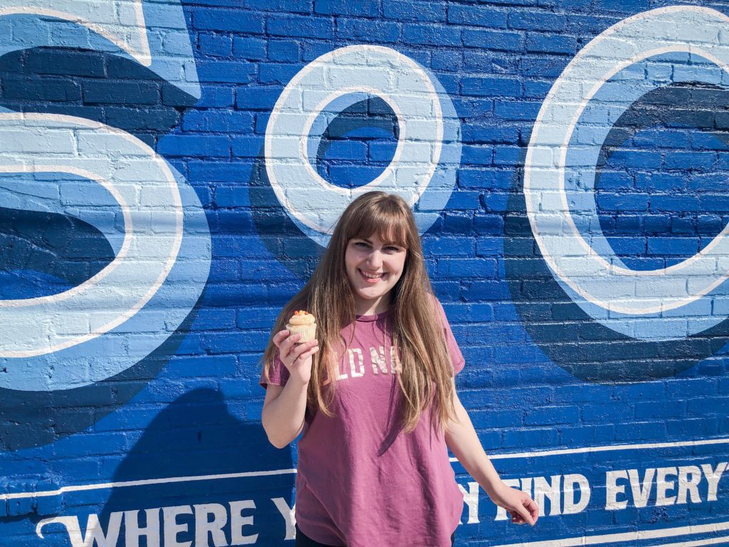 Girl in purple old navy t shirt with orange cupcake in front of blue soco wall mural in corinth, mississippi