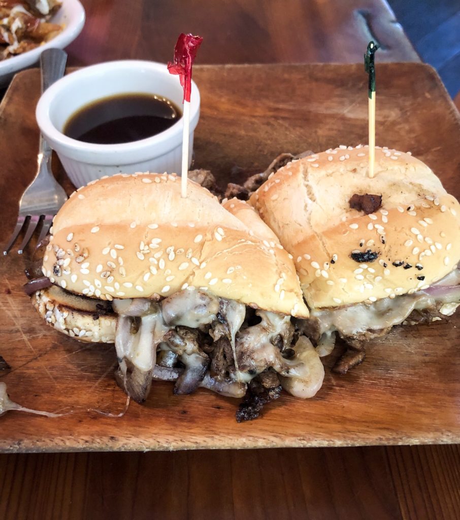 philly cheese steak sandwich on wood plate and table with dipping sauce at the outpost pickwick savannah tennessee